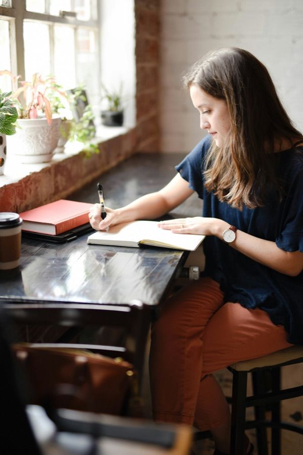 By a window, someone leans over a notebook, writing carefully